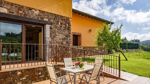 A patio with a table and chairs, a stone wall, and a view of a green landscape. - Apartment 'La Llosa' with Mountain Views, Private Terrace and Wi-Fi (Logrezana)