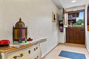 A hallway with a wooden door, a radiator, a glass-top table with a decorative item, and a blue mat on the floor. - Apartment 'La Llosa' with Mountain Views, Private Terrace and Wi-Fi (Logrezana)