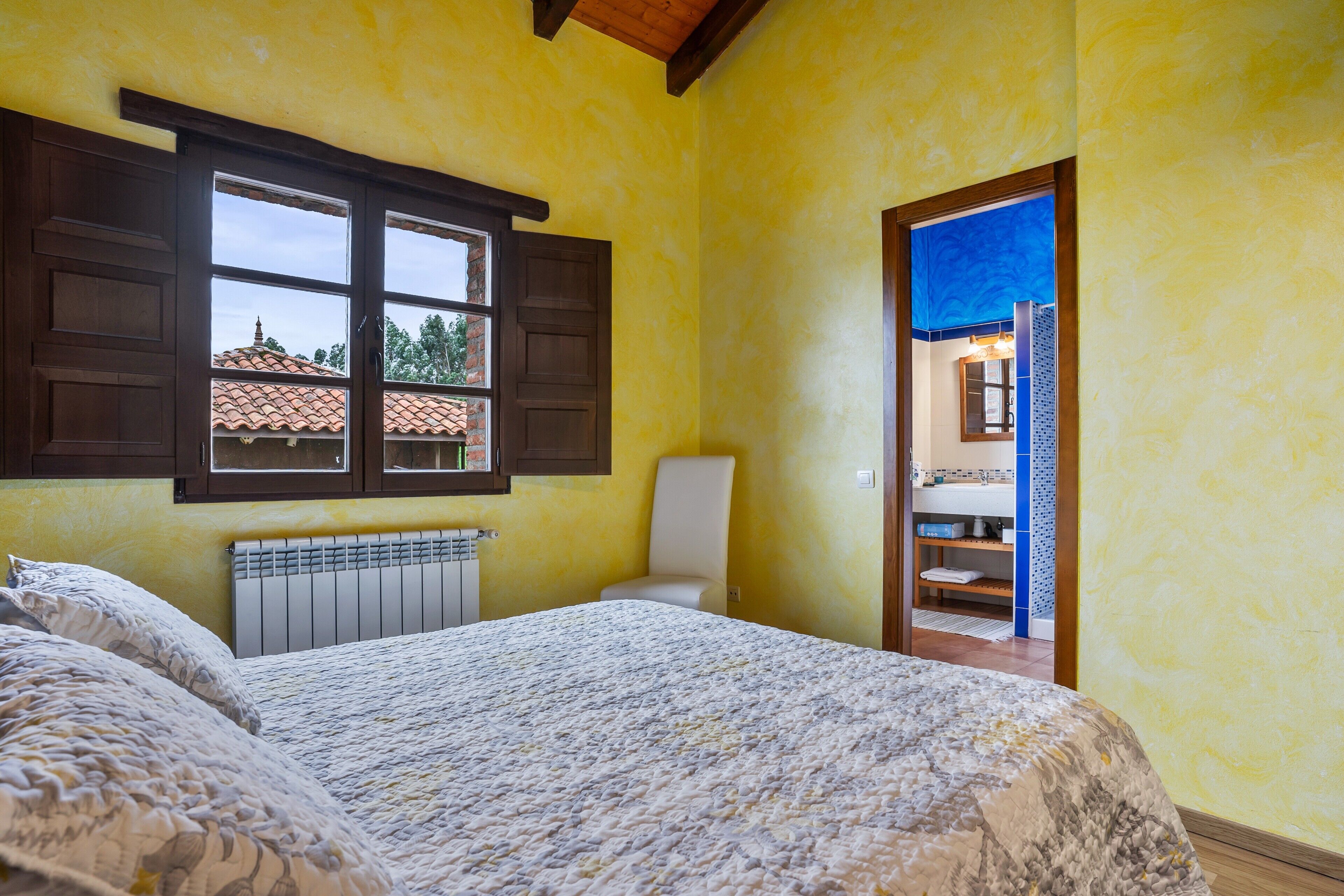 A bedroom with a bed, a radiator, a window with shutters, and a view of a building outside.