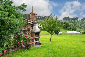 A rustic stone building with a chimney, surrounded by lush greenery and a clear sky. - Pedregal Farmhouse with Shared Terrace, Private Garden, and Wi-Fi (Gijon)