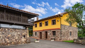 A two-story building with a stone facade and a yellow upper level, featuring a balcony and a stone wall. - Pedregal Farmhouse with Shared Terrace, Private Garden, and Wi-Fi (Gijon)