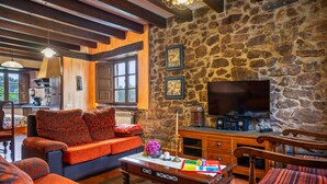 A cozy living room with a stone wall, a sofa, a coffee table, and a television. - Pedregal Farmhouse with Shared Terrace, Private Garden, and Wi-Fi (Gijon)