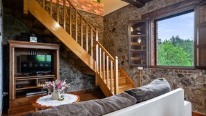 Un salon avec un mur en pierre, un escalier en bois, une télévision et un canapé.