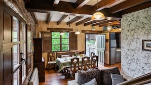 Un coin repas rustique avec des poutres en bois, une table dressée pour quatre personnes et une vue sur le jardin grâce à de grandes fenêtres.