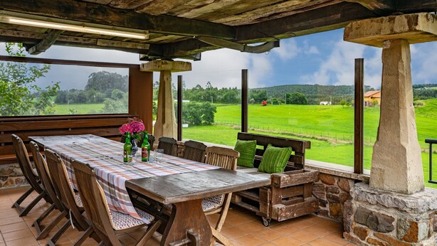 Un espace de restauration en plein air avec une table et des chaises en bois, un pilier en pierre et une vue sur un champ verdoyant.