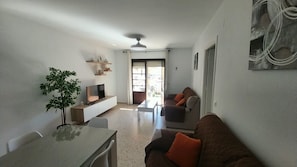 A modern living room with a TV, sofa, and dining table. - Apartment 'Chipiona Centro y Playa' with Private Terrace, Balcony and Wi-Fi (Chipiona)