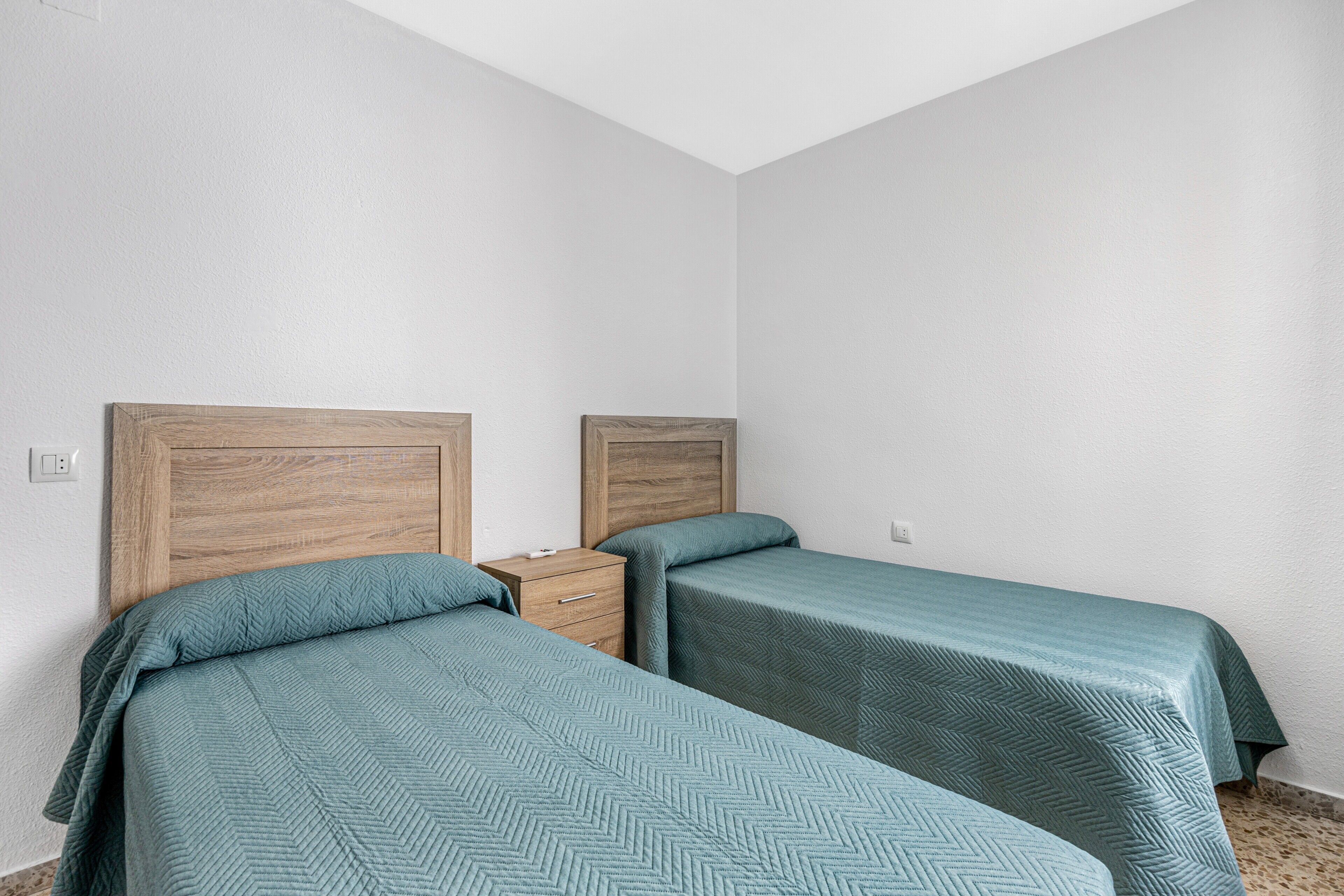 Una habitación con dos camas, cabeceros de madera, una mesita de noche y una pared blanca.