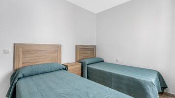 Una habitación con dos camas, cabeceros de madera, una mesita de noche y una pared blanca.