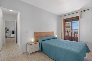 A bedroom with a bed, nightstands, a wooden headboard, a window with curtains, and a view of buildings. - Apartment 'Chipiona Centro y Playa' with Private Terrace, Balcony and Wi-Fi (Chipiona)