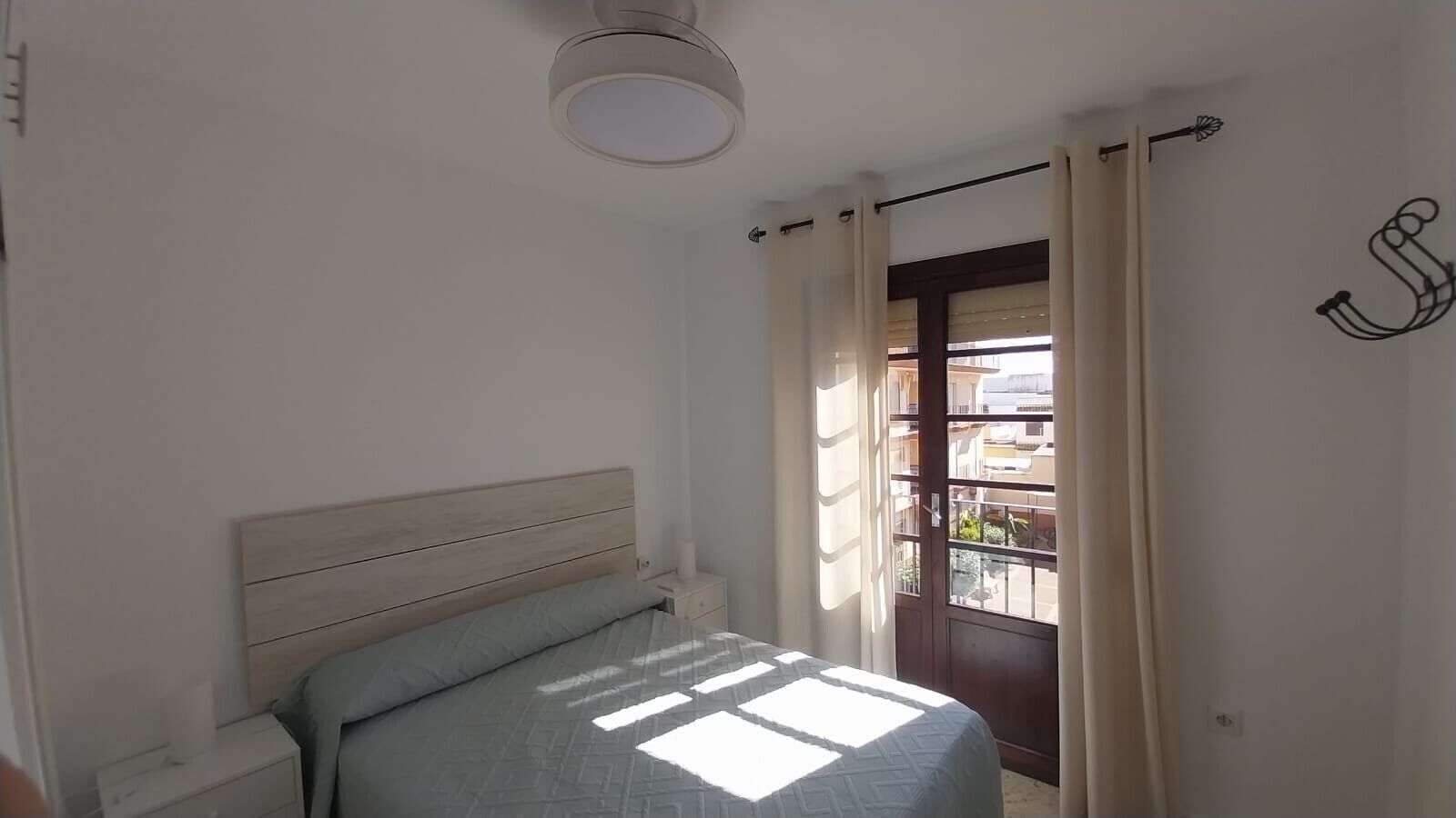 Een slaapkamer met een bed, nachtkastje, raam met gordijnen en uitzicht.