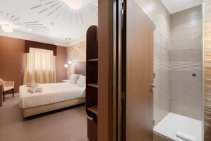 A hotel room with a bed, a desk, a chair, a shower area, and a wooden wardrobe.