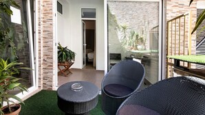 Un espace patio aménagé avec des meubles en osier, une plante en pot et une porte-fenêtre coulissante donnant sur un espace intérieur.