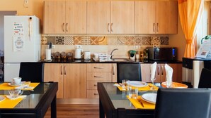 A compact kitchen with wooden cabinets, a refrigerator, a microwave, and a dining area with a table and chairs. - Room 'Quarto Casal Comfort Plus 104' with Shared Terrace, Wi-Fi and Air Conditioning (Faro)
