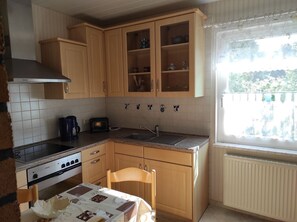 Cocina compacta con armarios de madera, cocina a gas, lavamanos y ventana con vistas al verdor.