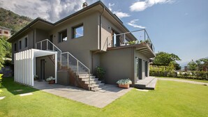 A modern two-story house with a balcony, a staircase, and a well-maintained lawn.