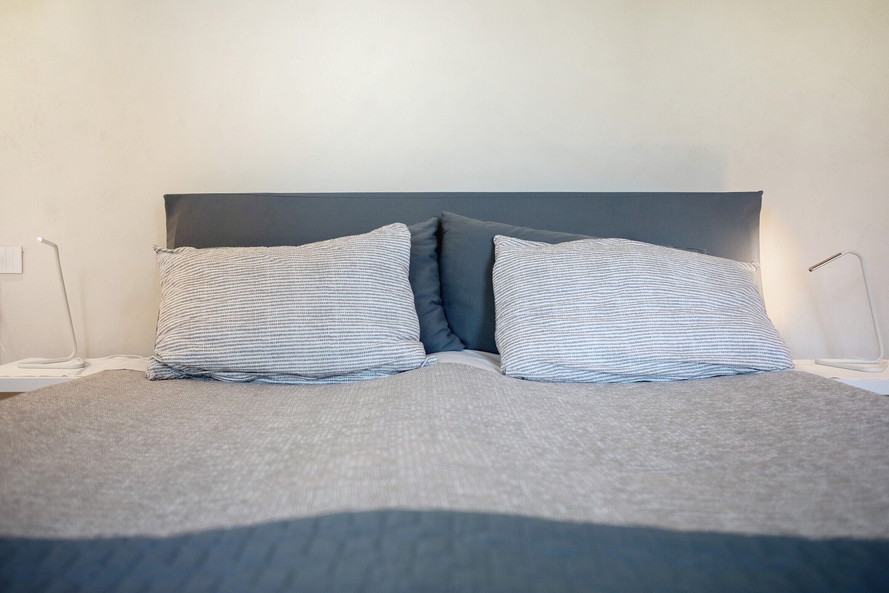 Ein Bett mit grauem Kopfteil, zwei Kissen und zwei Nachttische mit Lampen.