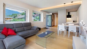 A modern living room with a grey sofa, a glass coffee table, and a dining area with white chairs.