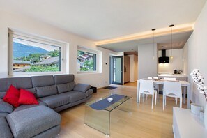 A modern living room with a grey sofa, a glass coffee table, and a dining area with white chairs.