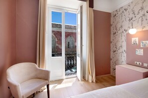 Une chambre dotée d’une porte-fenêtre coulissante donnant sur un balcon, d’un lit, d’une chaise et d’un bureau avec un luminaire.