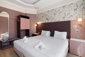A hotel room with a large bed, a wardrobe, a mirror, a nightstand, and a wall with floral wallpaper.