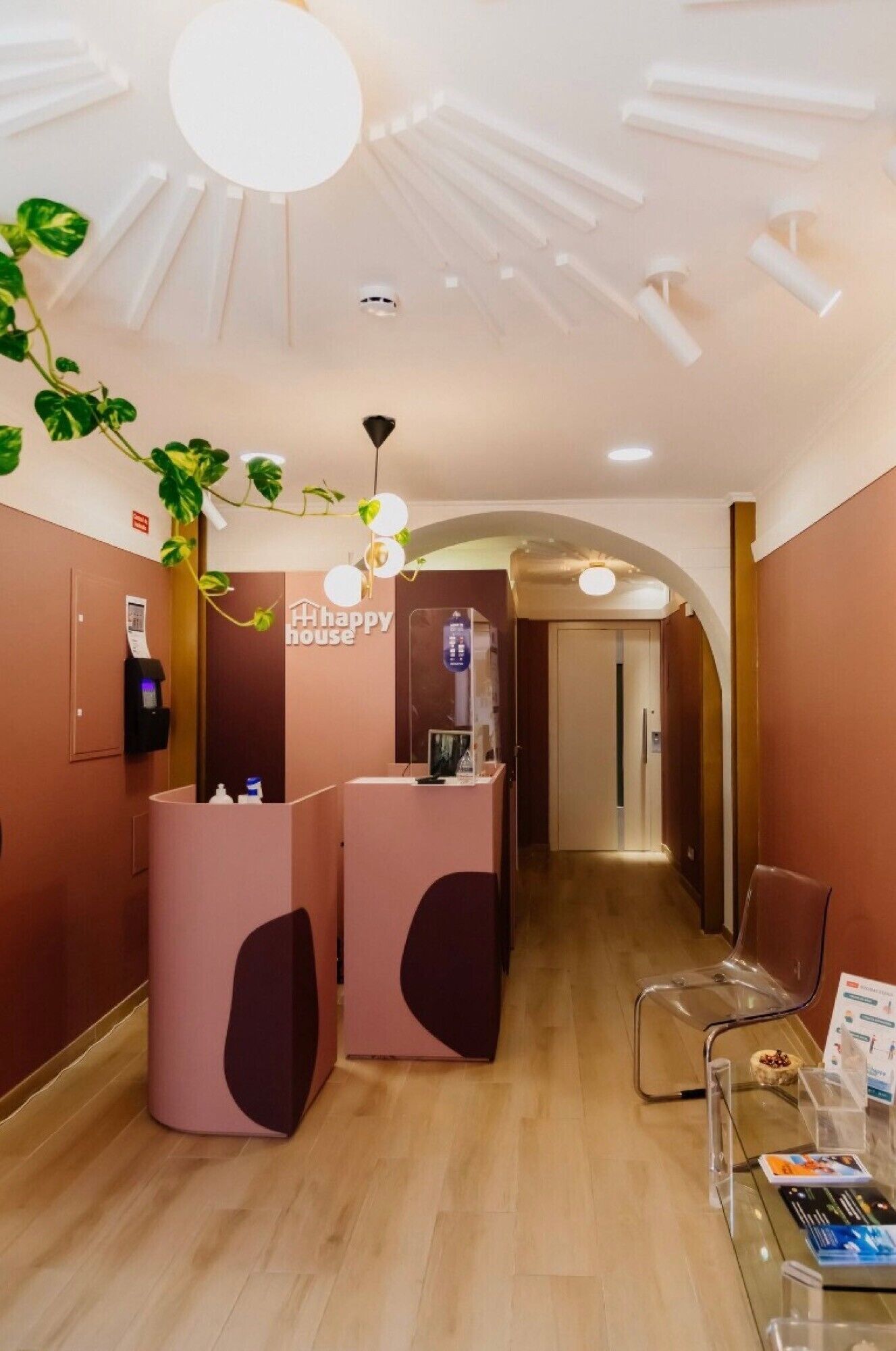 Un espace d’accueil au design moderne, comprenant un comptoir d’accueil, un espace d’attente avec des chaises et un plafond agrémenté d’un luminaire original.