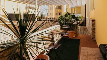 Une terrasse extérieure couverte, aménagée avec des meubles en bois, des plantes en pot et un mur en pierre.