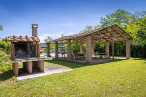A covered outdoor area with a barbecue grill, tables, and umbrellas. - Holiday Home 'Poggio2' with Shared Pool, Private Garden and Wi-Fi (Fauglia)