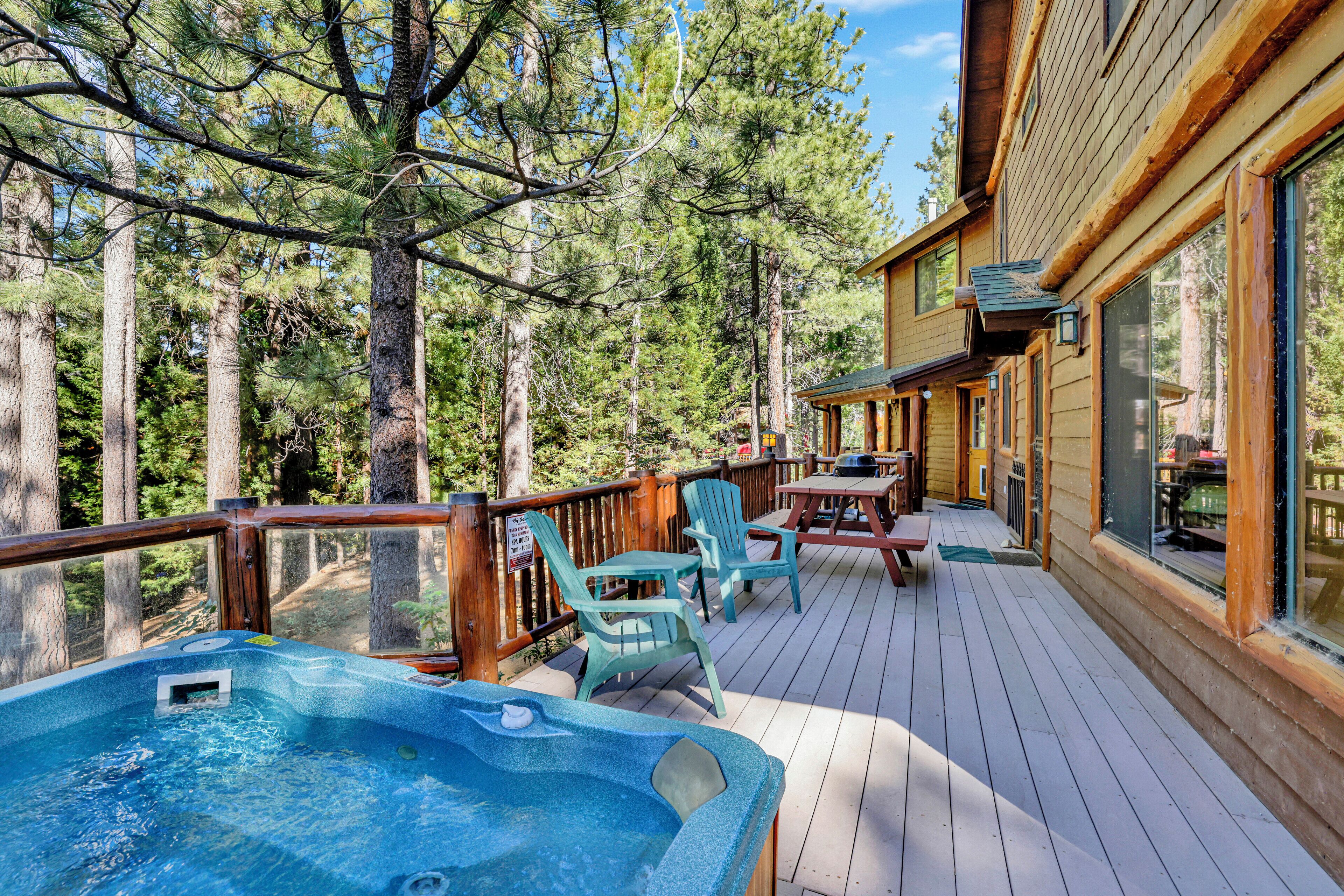 A wooden deck with a hot tub, outdoor seating, and a view of the forest.