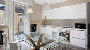 A modern kitchen with a glass dining table, white cabinets, and stainless steel appliances. - 'Surville' Apartment in Aosta with Mountain View and Balcony (Aosta)