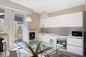 A modern kitchen with a glass dining table, white cabinets, and stainless steel appliances.