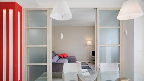 A modern living room with a glass table, white chairs, a grey sofa with red cushions, and a TV. - 'Surville' Apartment in Aosta with Mountain View and Balcony (Aosta)