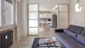 A modern living room with a sofa, a glass coffee table, and a view into the kitchen area. - 'Surville' Apartment in Aosta with Mountain View and Balcony (Aosta)