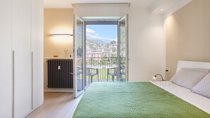 A bedroom with a green quilted bedspread, a white headboard, and a view of a balcony with chairs. - 'Surville' Apartment in Aosta with Mountain View and Balcony (Aosta)