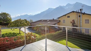 Un balcón con vistas a una montaña, una casa con techo de tejas y cielo despejado.