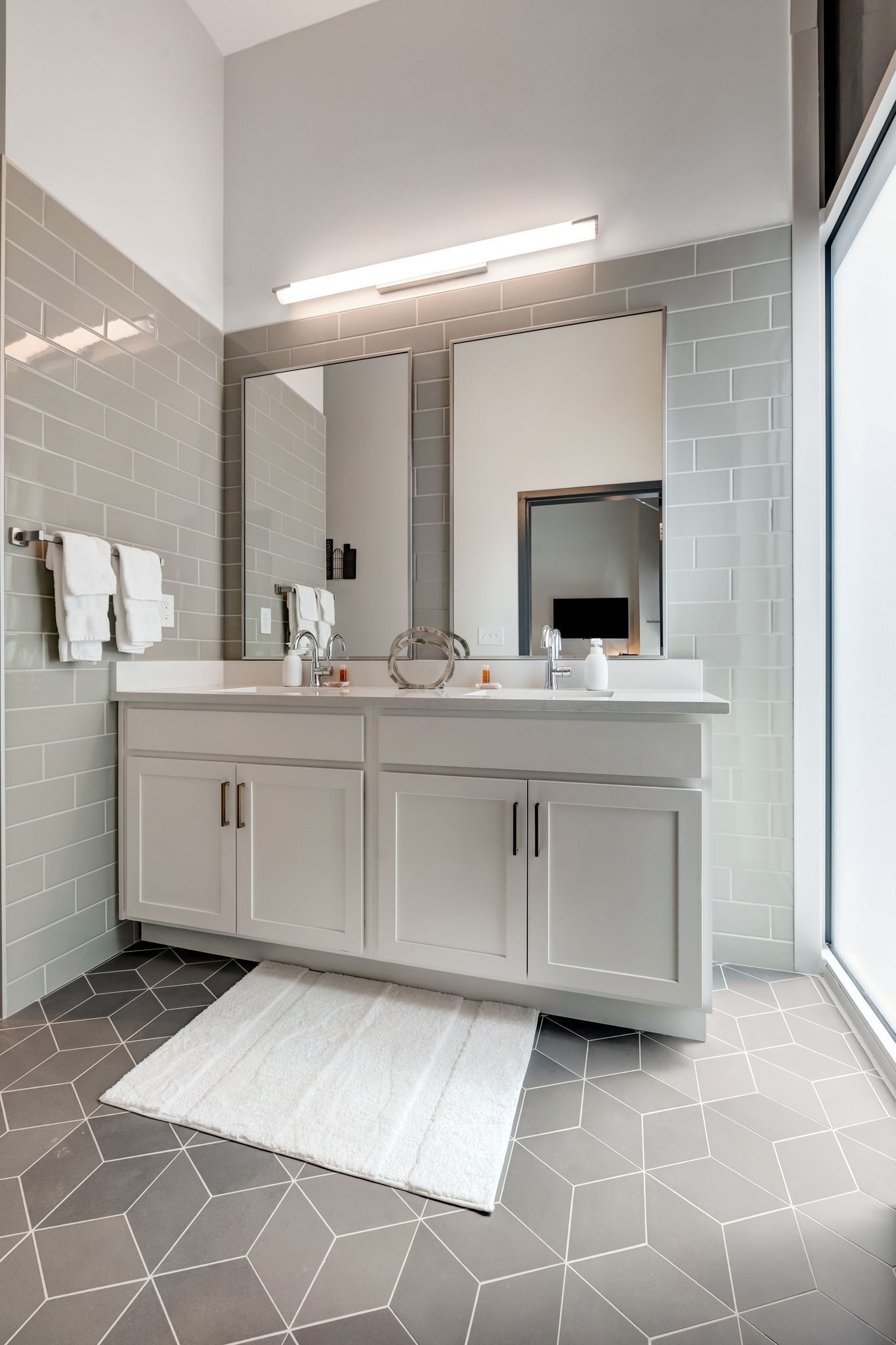 Une salle de bain moderne avec un grand miroir, des meubles blancs et un sol à motifs géométriques.