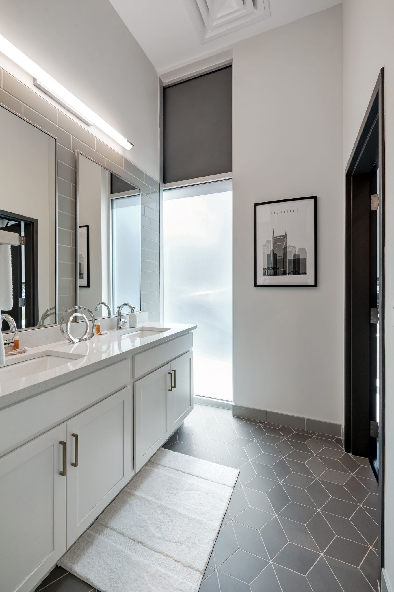 A modern bathroom with two sinks, a large mirror, and a cityscape poster on the wall.