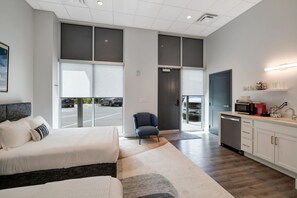 A modern hotel room with a large bed, a seating area, a kitchenette, and a view of the parking lot. - Corporate Suite: Two Queen Edition (Nashville)
