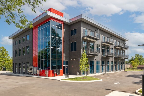 A modern building with a red and grey facade, large windows, and a parking lot. - Corporate Suite: Two Queen Edition (Nashville)