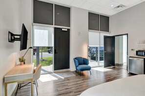 A modern hotel room with a large window, a desk with a chair, a blue armchair, and a small kitchenette. - Brand New Professionals Paradise (Nashville)