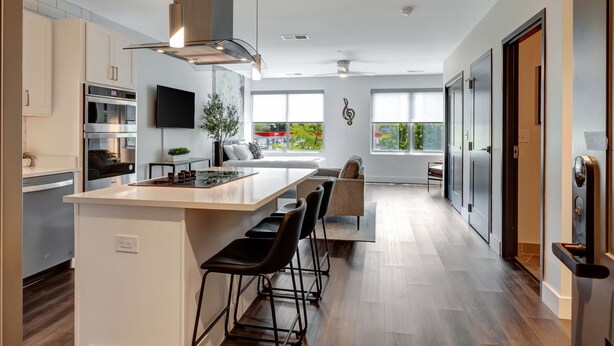 Een moderne keuken met een centraal eiland, barkrukken, een flatscreen televisie en een groot raam met uitzicht op groen.