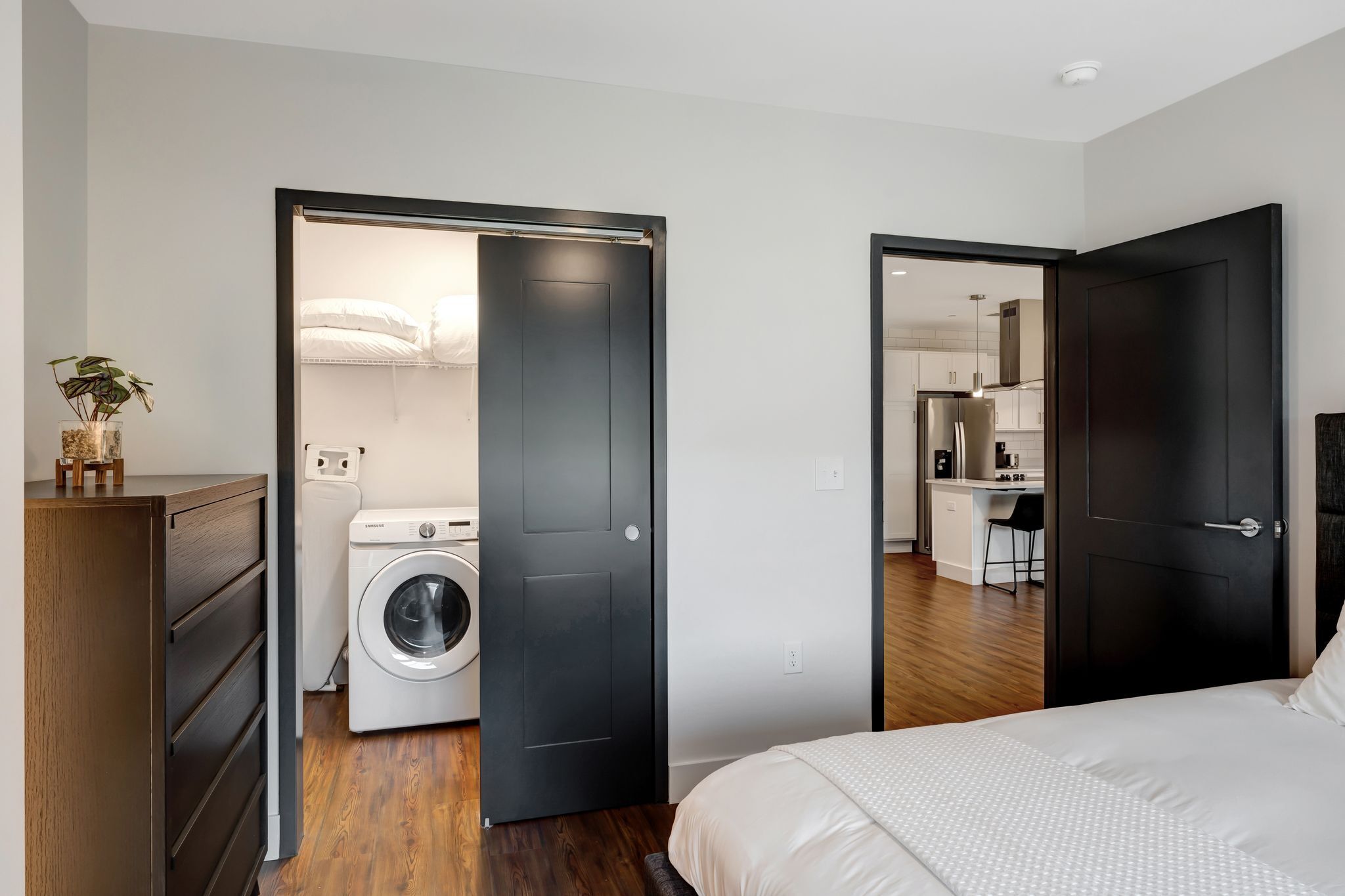 Un dormitorio moderno con una cama grande, una lavadora y una kitchenette en la habitación contigua.