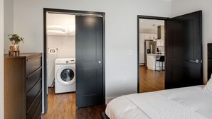 Un dormitorio moderno con una cama grande, una lavadora y una kitchenette en la habitación contigua.