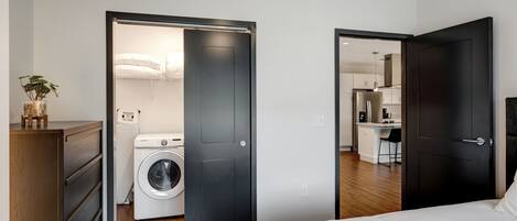 Un dormitorio moderno con una cama grande, una lavadora y una kitchenette en la habitación contigua.
