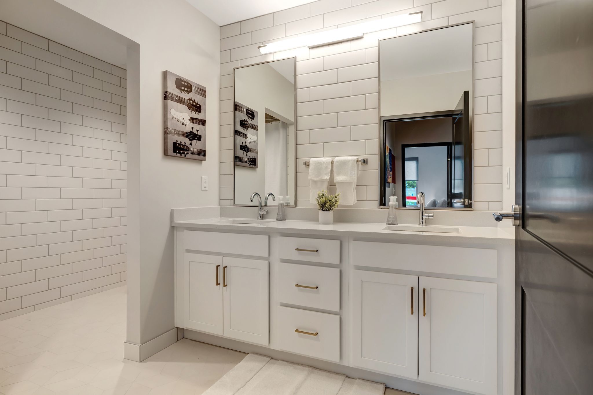 Une salle de bain moderne avec des meubles blancs, un grand miroir et un réfrigérateur en acier inoxydable.
