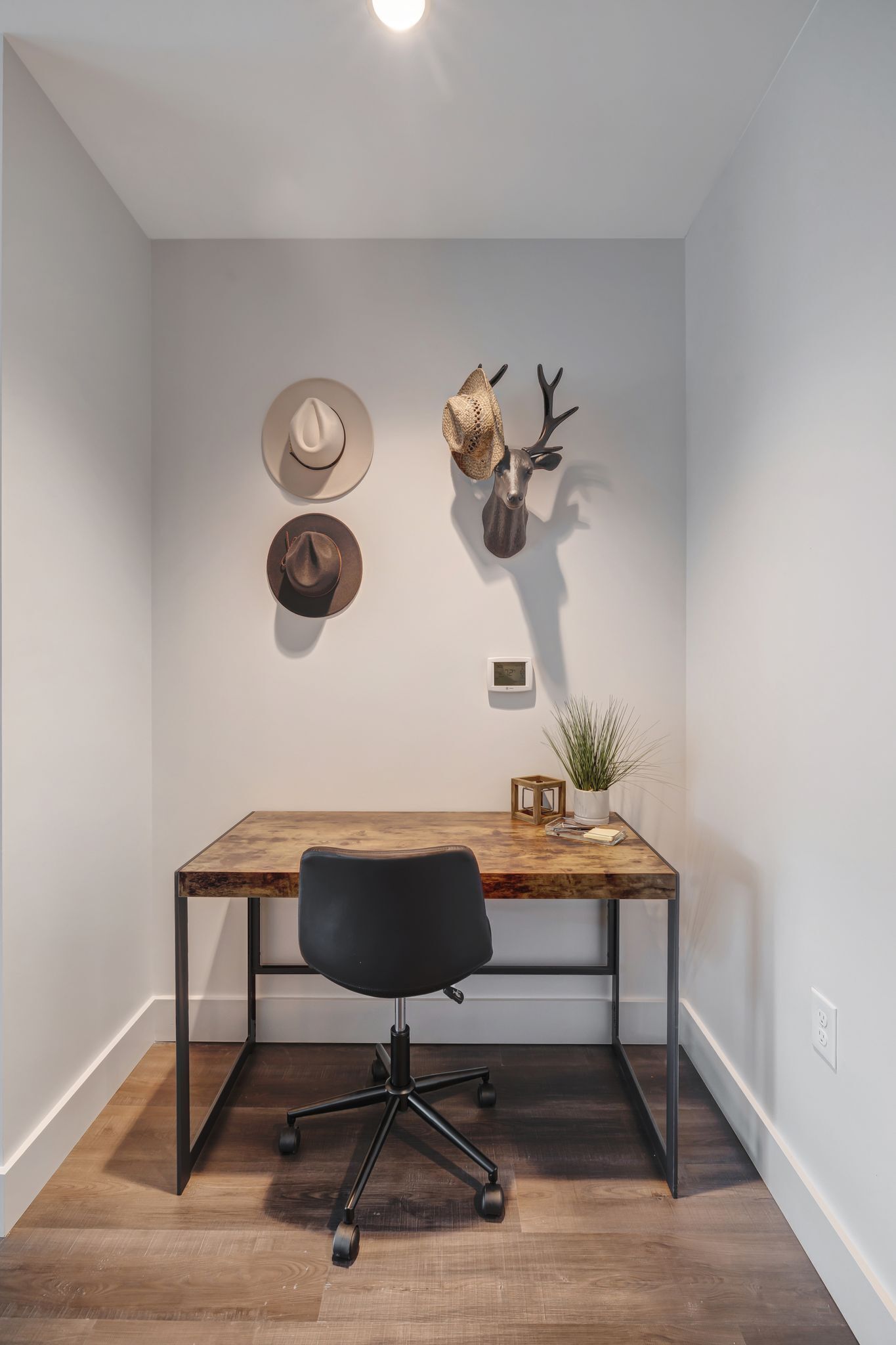 A room with a wooden desk, black office chair, and two hats on the wall.