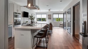Una cocina moderna con una isla central, taburetes de bar y un ventanal con vistas al exterior.