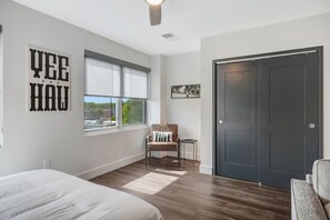Une chambre avec un grand lit, une chaise, une porte sombre et une fenêtre avec des stores.