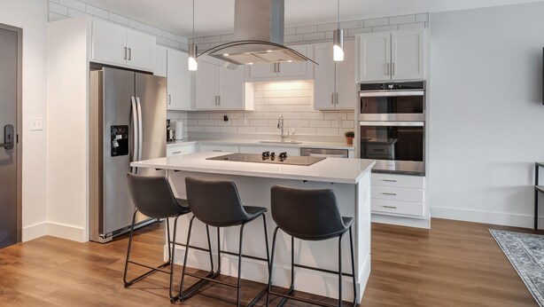 Una cocina moderna con una isla central, electrodomésticos de acero inoxidable y taburetes de bar.