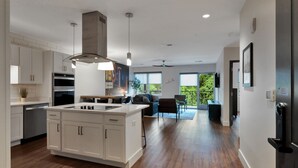 A modern kitchen with white cabinetry, a central island, and a dining area with a view of greenery. - Neon Nest: One Bedroom Nashville Getaway (Nashville)