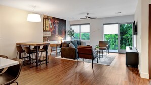 A spacious living area with a dining table, chairs, a sofa, and a large window with a view of greenery. - Neon Nest: One Bedroom Nashville Getaway (Nashville)